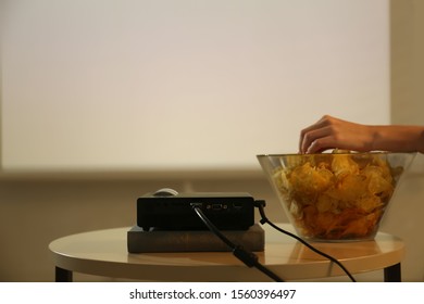 Woman Eating Chips While Watching Movie Using Video Projector At Home, Closeup