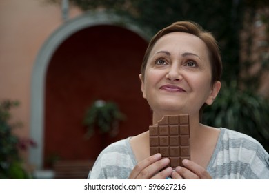 Woman Eating Chocolate. Portrait Of Happy Middle Aged Female Eating Sweets And Daydreaming Looking Up With A Happy Smile