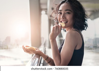 Woman Eating Crispy Chips Snack In Hand In The City Sunset Background