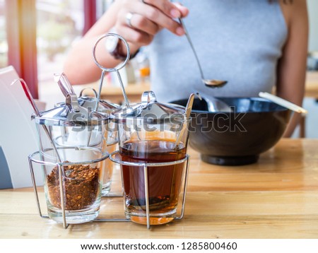 Woman eating a cup of noodles with Thai-style noodles seasoning set, cayenne pepper, sugar, fish sauce, and vinegar on wooden table.