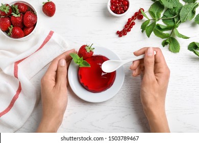 Woman eating delicious fresh red jelly at white wooden table, top view