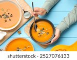 Woman eating delicious pumpkin soup at light blue wooden table, top view