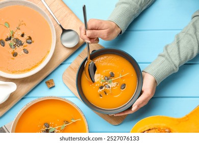 Woman eating delicious pumpkin soup at light blue wooden table, top view