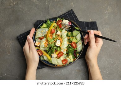 Woman Eating Delicious Salad With Lentils, Vegetables And Cheese At Grey Table, Top View