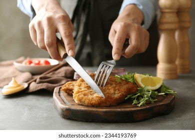 Woman eating delicious schnitzel with lemon and microgreens at grey table, closeup
