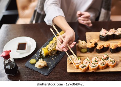 Woman eating and enjoying fresh sushi in luxury restaurant. Female client holding food sticks and eating oriental meal on lunch. Traditional Japanese dish coming with wasabi. Concept of food.