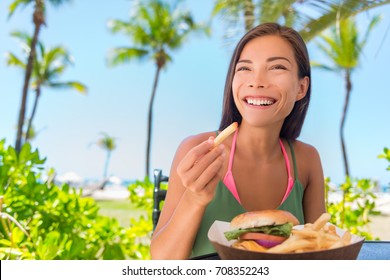 Woman Eating French Fries Food At Resort Restaurant. Asian Girl Enjoying Summer Vacation At Beach Bar With Fast Food Lunch Meal, Burger And Fries.