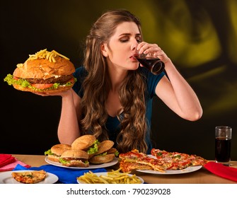 Woman Eating French Fries And Hamburger With Pizza. Portrait Of Student Consume Fast Food On Table. Girl Trying To Eat Junk On Dark Background. Disruption From Diet.