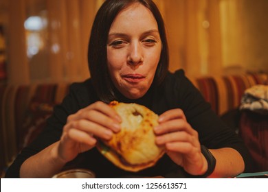 Woman Eating French Hamburger. Portrait Of Student Consume Fast Food On Table. Girl Trying To Eat Junk. Advertise Fast Food On Daek Background. Student Eats Semi-finished Products.
