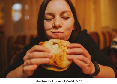 Woman Eating French Hamburger. Portrait Of Student Consume Fast Food On Table. Girl Trying To Eat Junk. Advertise Fast Food On Daek Background. Student Eats Semi-finished Products.
