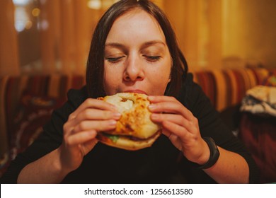 Woman Eating French Hamburger. Portrait Of Student Consume Fast Food On Table. Girl Trying To Eat Junk. Advertise Fast Food On Daek Background. Student Eats Semi-finished Products.
