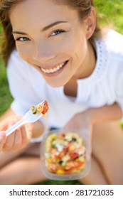 Woman Eating Gluten Free Pasta Salad. Portrait Of Girl Eating Lunch Takeaway In Park Outdoors. Biracial Asian Caucasian Female Model In Her Twenties Smiling Happy Looking At Camera.