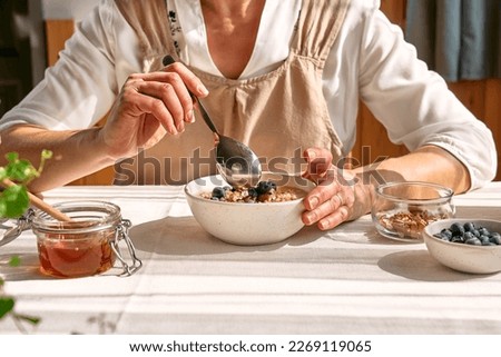 Woman eating healthy dieting vegan nutritious breakfast. Female hand holding spoon over the bowl with oatmeal porridge with walnuts, blueberries and honey.