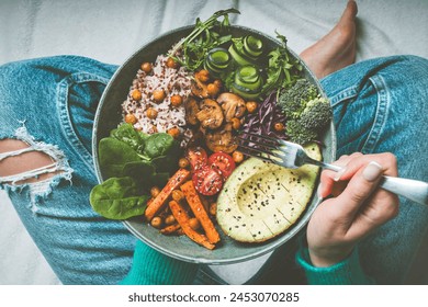 Woman eating healthy meal. Bowl with rice, quinoa, avocado, cucumber, broccoli and cucumber. Healthy diet, lunch or dinner. Healthy food plate