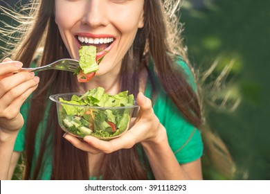 Woman eating healthy salad from plastic container over green grass with flying hair on a sunny spring day. backlight - Powered by Shutterstock