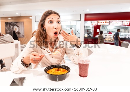 A woman eating too hot and peppery soup in an Asian fast food restaurant. Concept of spices in Oriental cuisine