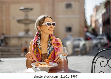 Woman eating italian pasta and drinking wine at restaurant on the street in Rome. Concept of Italian gastronomy and travel. Stylish woman with sunglasses and colorful hair shawl - Powered by Shutterstock