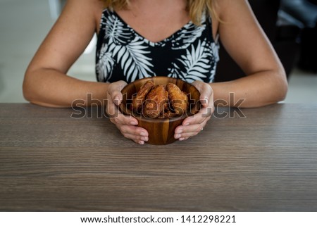 A woman eating Korean spicy chicken wings from a wooden bowl