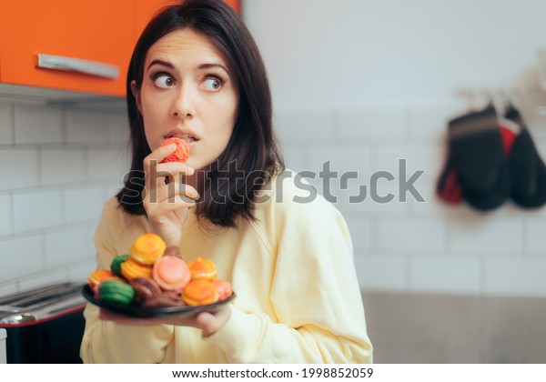Woman Eating Macarons Feeling Guilty and Hiding.\
Adult person with sugar addiction hiding her alimentary habits over\
indulging because of\
stress\

