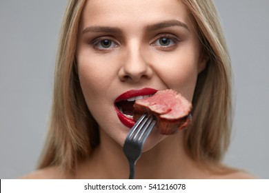 Woman Eating Meat. Closeup Of Healthy Hungry Girl With Beautiful Face, Red Lips Eats Delicious Grilled Meat. Female Mouth Biting Piece Of Tasty Beef Steak On Fork. Nutrition Concept. High Resolution