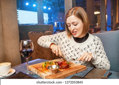 Woman eating meat steak and drinking wine in a restaurant in a nightclub