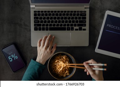 Woman Eating Noodle while Working on Computer Laptop, Mobile Phone and Tablet. Top View. Unhealthy Food in a Busy Working Day. a Workaholic Habits - Powered by Shutterstock