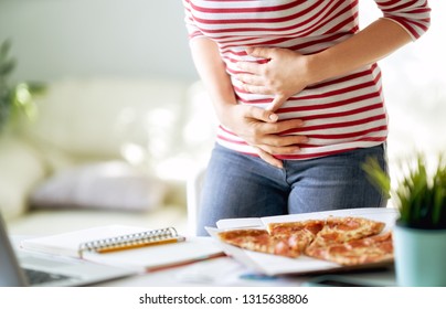 Woman Eating Pizza On The Desk At Work And Having Stomach Problems.