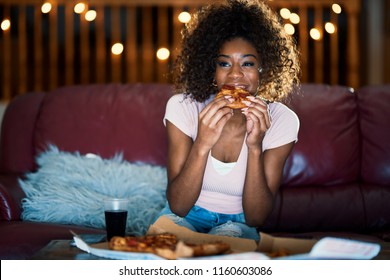 woman eating pizza and watching tv late at night on sofa