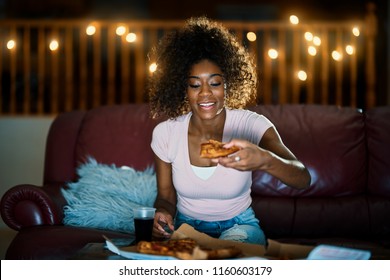 Woman Eating Pizza And Watching Tv Late At Night On Sofa