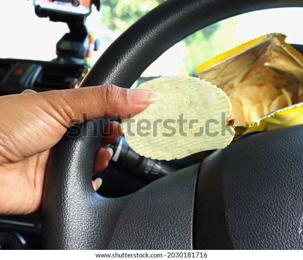 Woman eating\
potato chips in bag on hand and\
car