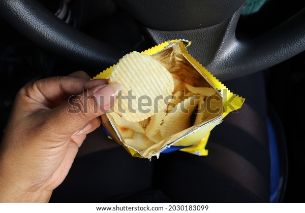 Woman eating
potato chips in bag on hand and
car