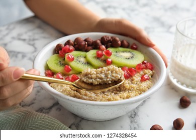 Woman Eating Quinoa Porridge With Hazelnuts, Kiwi And Pomegranate Seeds At Marble Table, Closeup