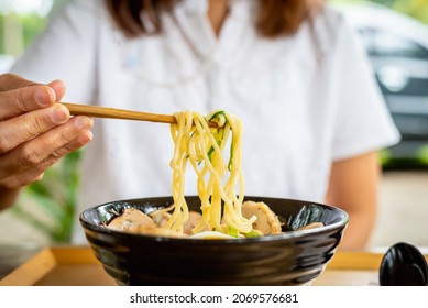 Woman Eating A Ramen Japanese Noodle Soup In A Black Color Ramen Bowl.