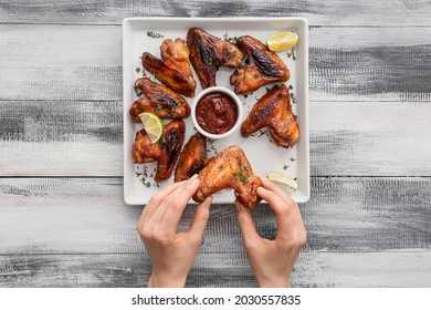 Woman Eating Roasted Chicken Wings On Wooden Background