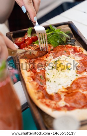 Woman is eating rome pizza with pepperoni, tomatoes and fried egg on a summer terrace
