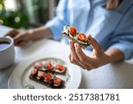 Woman eating rye crusty bread with creamy vegan tofu cheese, cherry tomatoes and greens rucola. Healthy wholesome food, gluten-free, quick healthy snack, diet concept. 