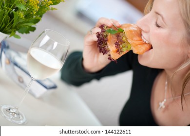 Woman Eating Salmon Slices On Bread In Restaurant