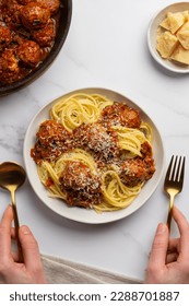Woman eating spaghetti pasta with meatballs in tomato vegetable sauce, sprinkled with parmesan cheese, holding cutlery. View from above.