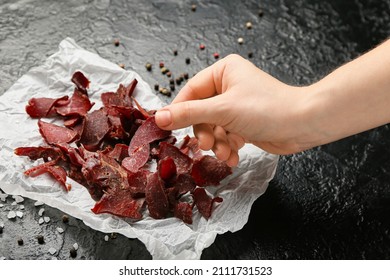 Woman Eating Spicy Beef Jerky On Dark Background