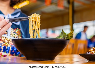 Woman Eating A Spicy Ramen Japanese Noodle Soup In A Black Color Ramen Bowl.