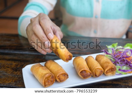 Woman eating spring rolls by using hand.
