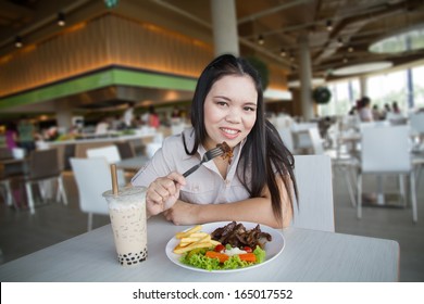 Woman eating steak in a food center.
