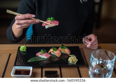 Woman eating sushi in the black plate on a wooden table. Hands of the girl close-up.
