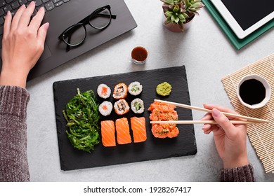 Woman eating sushi takeaway at work desk and working overhead. Eating sushi for lunch break, lunch meal at work, eating at work