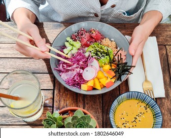 Woman eating tasty colorful healthy natural organic vegetarian Hawaiian poke bowl using asian chopsticks on rustic wooden table. Healthy natural organic eating concept. - Shutterstock ID 1802646049