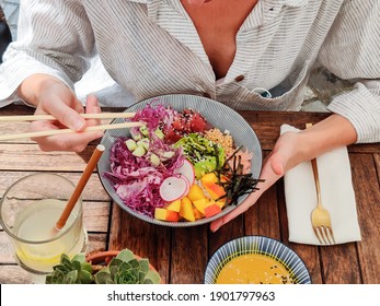 Woman Eating Tasty Colorful Healthy Natural Organic Vegetarian Hawaiian Poke Bowl Using Asian Chopsticks On Rustic Wooden Table. Healthy Natural Organic Eating Concept.