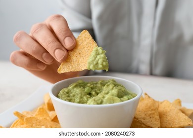 Woman Eating Tasty Guacamole With Nachos On Light Table, Closeup