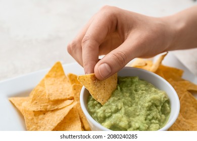 Woman Eating Tasty Guacamole With Nachos On Light Background, Closeup