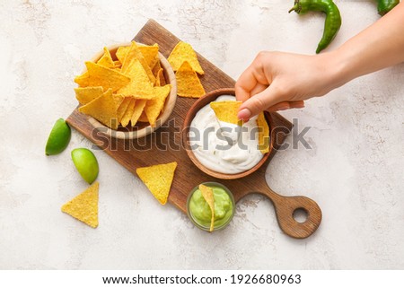 Woman eating tasty nachos with sauces on light background