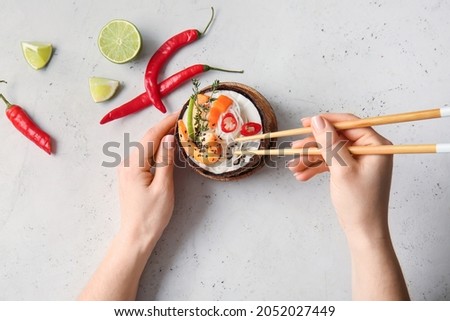 Woman eating Thai noodle soup on light background